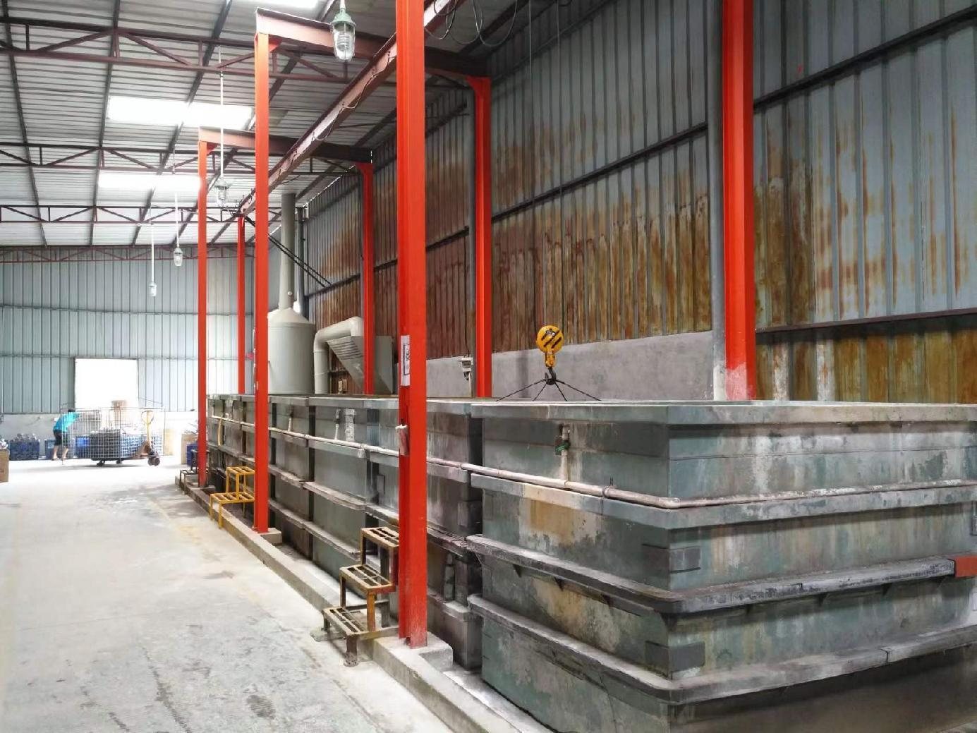 Rows of large open pretreatment tanks with an overhead hoist and extraction ducting running the length of the bay