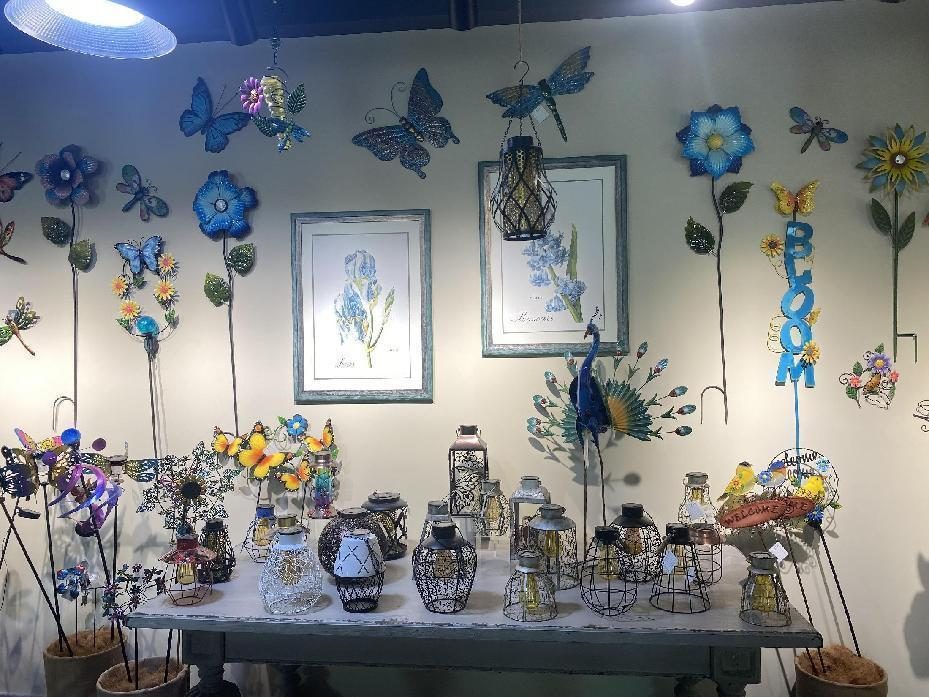 A wall of metal butterflies and flower stakes above a table of lanterns and planters